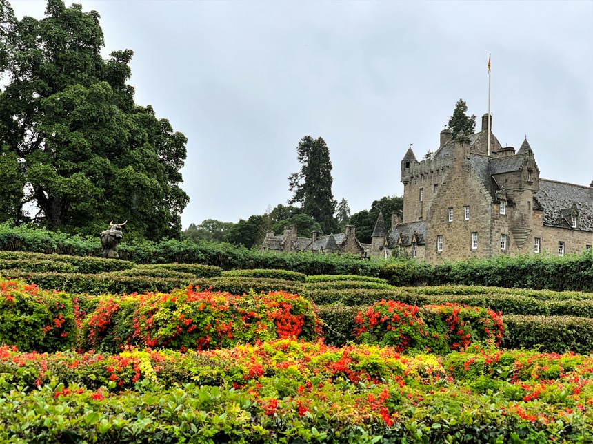 Beautiful gardens with green manicured bushes surround the stone Cawdor Castle, seen from the Classic Scotland Barge Cruise.