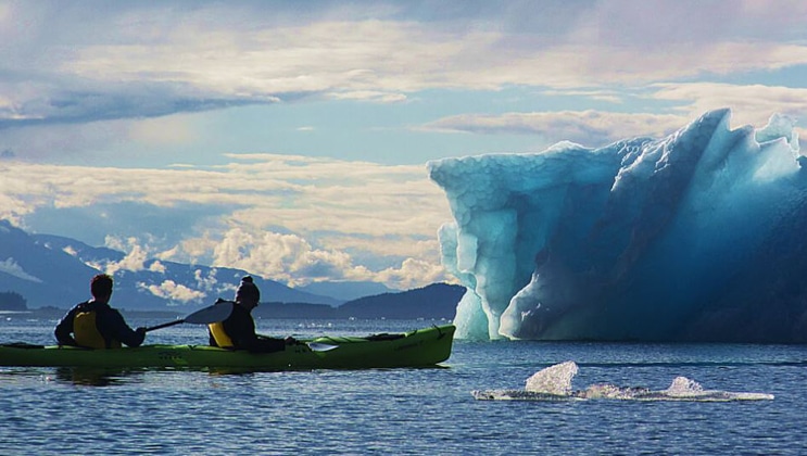 A pair of tandem kayakers paddles up to an icy blue iceberg bit during the Glacier Bay Outer Coast Expedition.