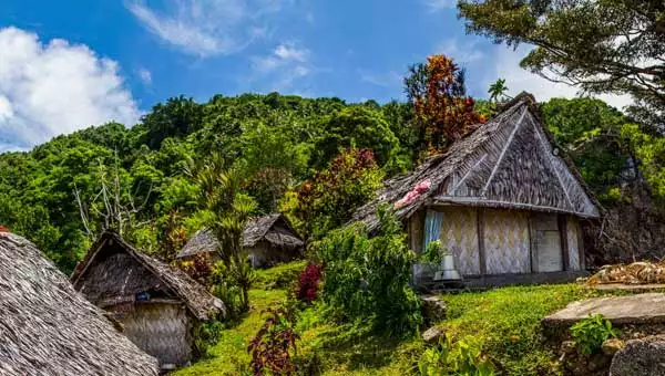 Thatch-roof huts line a lush green hillside on a sunny day during a South Pacific vacation.