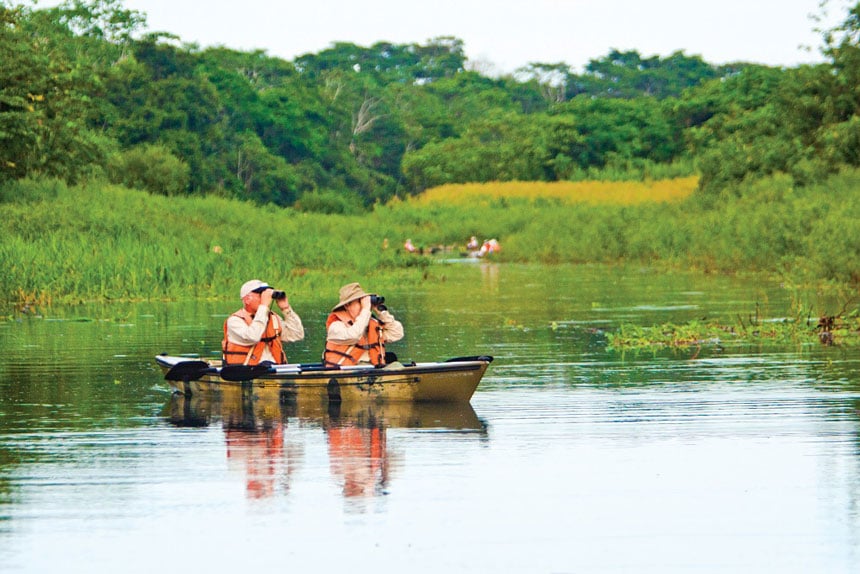 Amazon birders use binoculars from a tandem kayak to watch for wildlife in a calm tributary.