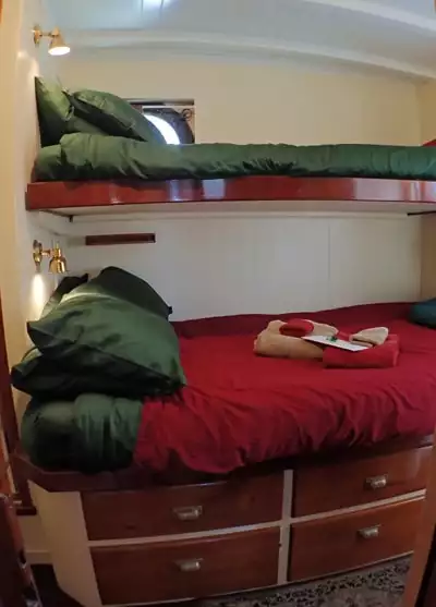 Cabin #1 aboard Catalyst small ship. A bunk bed against a white wall, porthole window and green and red bedding and pillows.