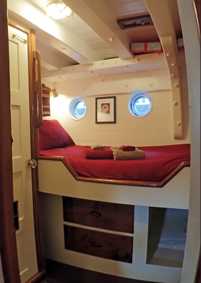 Cabin 2 aboard Catalyst, small ship in Alaska. Two porthole windows above a single mattress wrapped in red bedding and pillows.