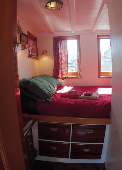 Cabin #6 aboard small ship Catalyst. Two windows above a bed with red and green bedding sitting on top of 4 cabinets.