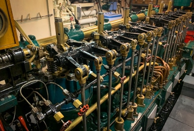 The engine room aboard small ship Catalyst, with a row of green and gold colored machinery parts