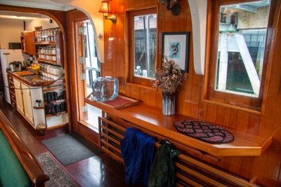 The galley aboard smalls ship Catalyst, brown glossy wood with shelfs, a seating area and small kitchen