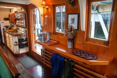 The galley aboard smalls ship Catalyst, brown glossy wood with shelfs, a seating area and small kitchen