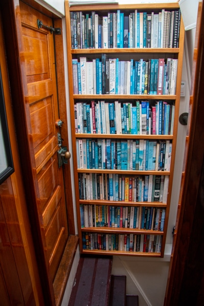 A book shelf filed with books sits at the top of a steep staircase leading to the lower deck of Alaska small ship Catalyst
