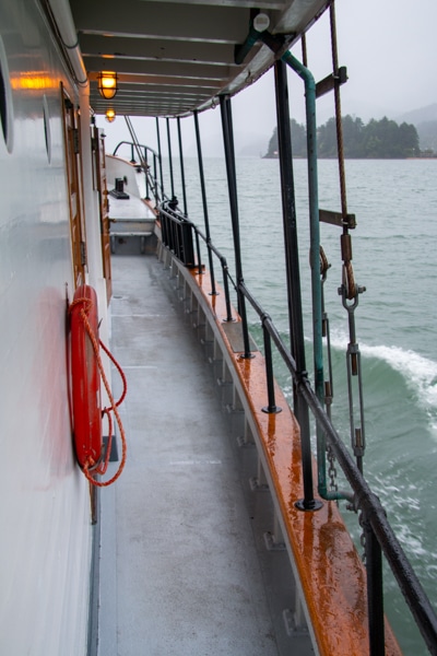 Looking out over a rainy Alaska landscape from the outer walk way that surrounds the main deck of Alaska small ship Catalyst.
