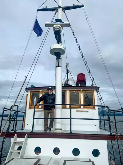 An Alaska cruise passenger standing on the top deck of the Catalyst small ship in front of the pilot house.