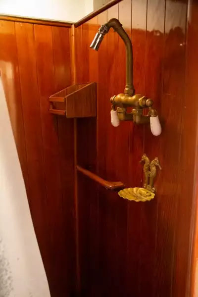 The private shower inside a cabin aboard Alaska small ship Catalyst. A brown wood shower with bronze shower head and soap dish.