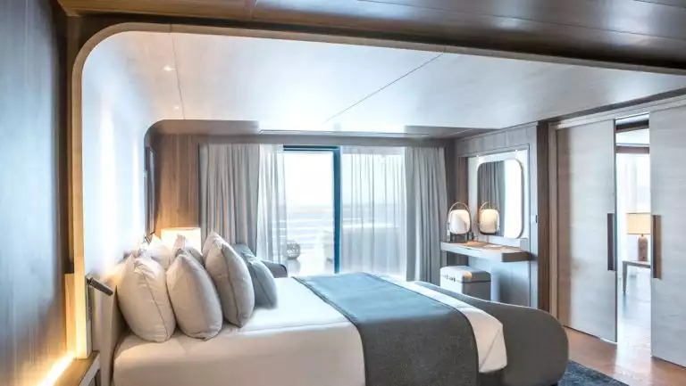 Owner's Suite aboard Le Commandant Charcot ship, with beige & blue color theme, double bed, couch, TV & private balcony.
