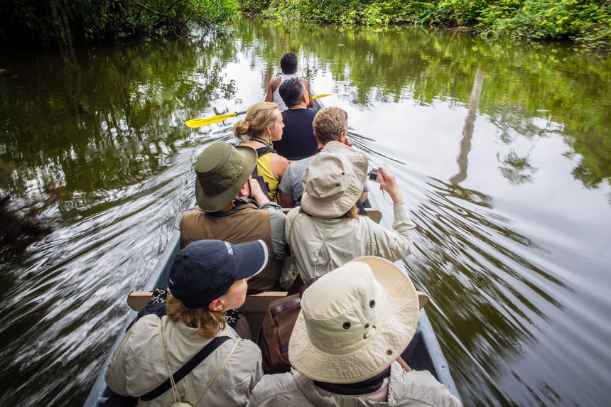 Amazon travelers glide through glassy water in a canoe with bench seats, spotting for wildlife.