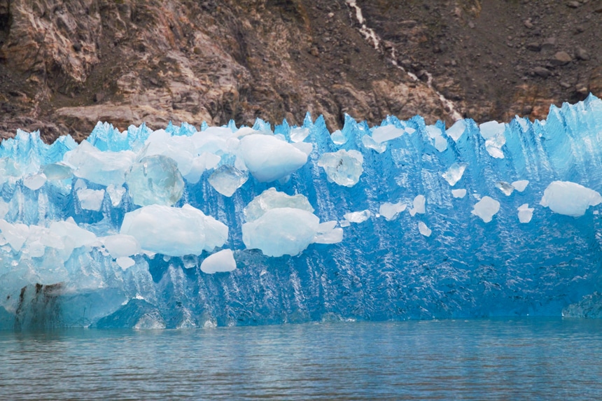 A long bright teal crystal-like jagged ice berg floating in the Inside Passage seen from an Alaska cruise abord Catalyst ship