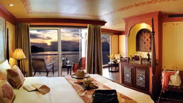 Upscale suite aboard a luxury Southeast Asia tour, with private veranda overlooking a sunset, Moroccan decor, tea service set on a 4-poster bed & a wet bar.