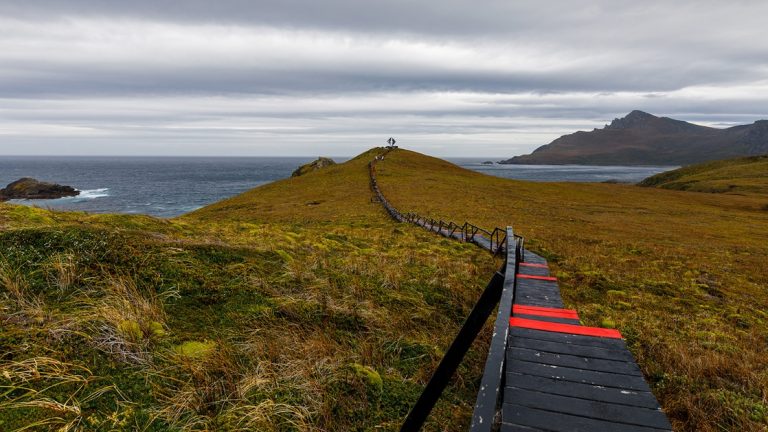 Wooden walkway painted black & red leads out to a silver statue at Cape Horn during the Essential Patagonia: Chilean Fjords & Torres del Paine Cruise.