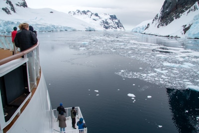 guests gather on the bow and observation wing to take in the view of floating icebergs and snowy mountain landscape of Antarctica,