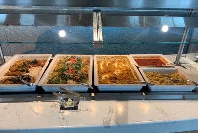 Food buffet selection aboard Greg Mortimer ship, white large serving plates set next to each other hold colorful menu items.