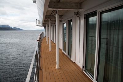 The wrap around outside walkway on the deck aboard Greg Mortimer luxury Antarctica ship, wooden floor with handrails infront of glass cabin doors.