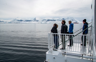 A group stand on the lowered hydraulic platform that extends from the side of the Greg Mortimer ship and look out over the Antarctic landscape.