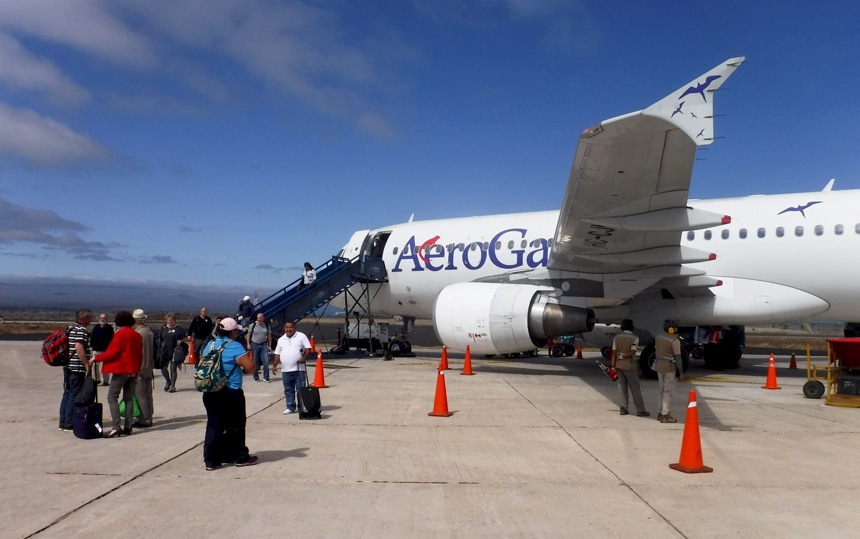 En la pista del aeropuerto, los viajeros de Galápagos con su equipaje esperando para abordar un avión blanco con la etiqueta Aero Galapagos. 