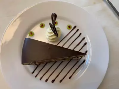 Slice of deletant chocolate cake on a white plate decorated with lines of chocolate served for dessert aboard Greg Mortimer ship.