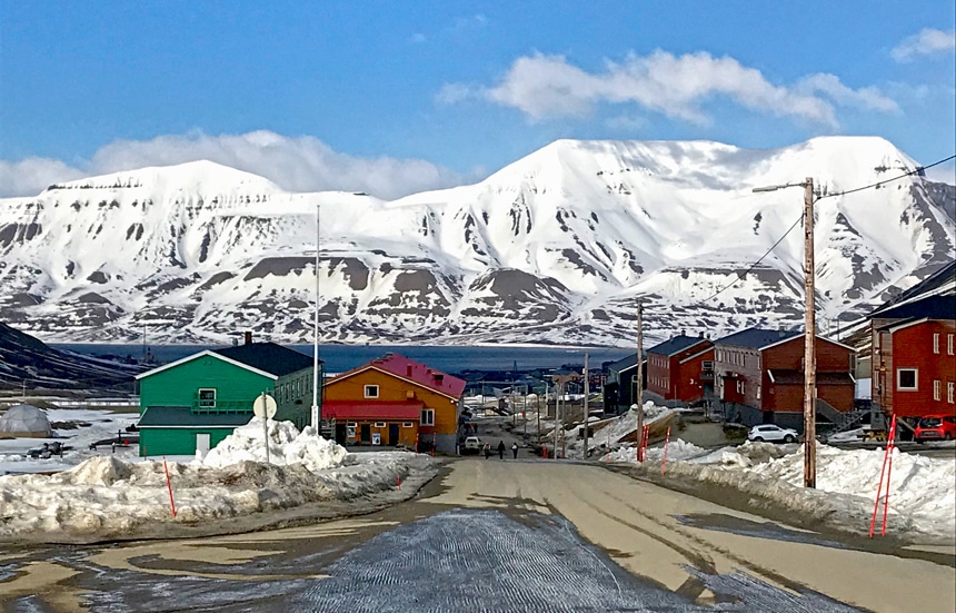 The town of Longyearbyen on Spitsbergen Island has brightly colored buildings sit in front of a massive snowy mountain range.