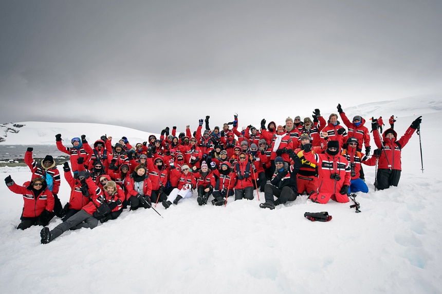 A group photo of cruise passengers during a shore excursion in Antarctica, all wearing the same red winter parka.