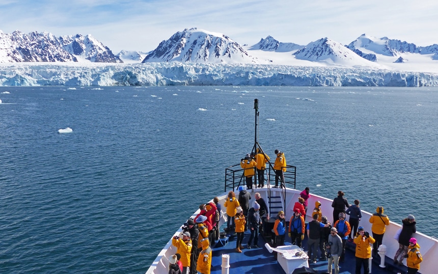 Arctic cruise passengers gather at the bow of the ship to take in the views of the sprawling massive ice shelf in Svalbard.