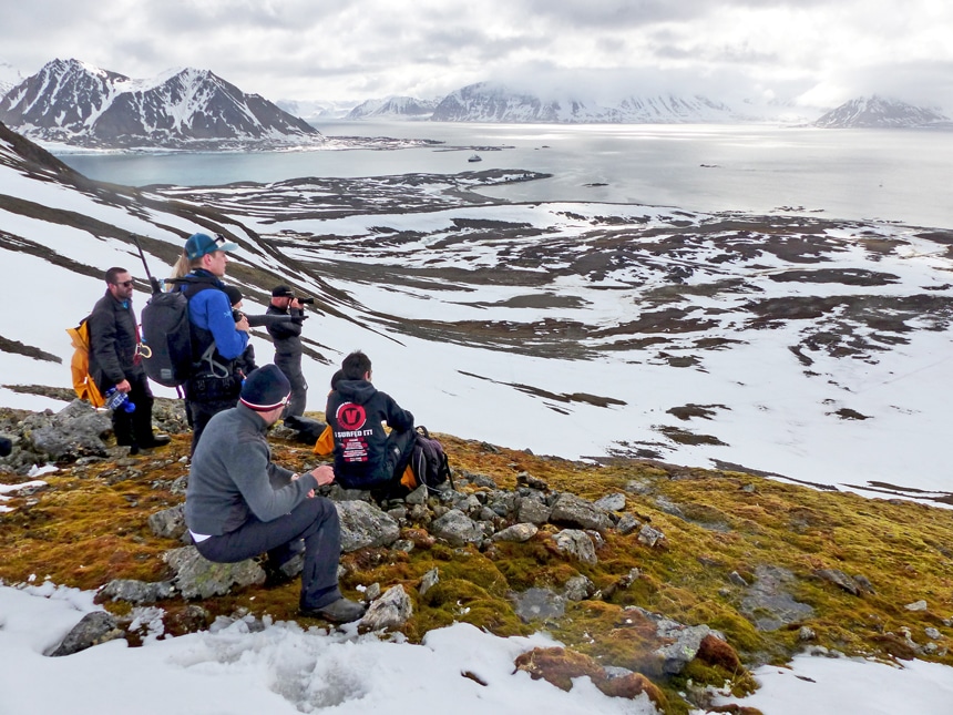A group hiked to a view point during a shore excursion of their Arctic Svalbard cruise, they look out over the snowy landscape below them.