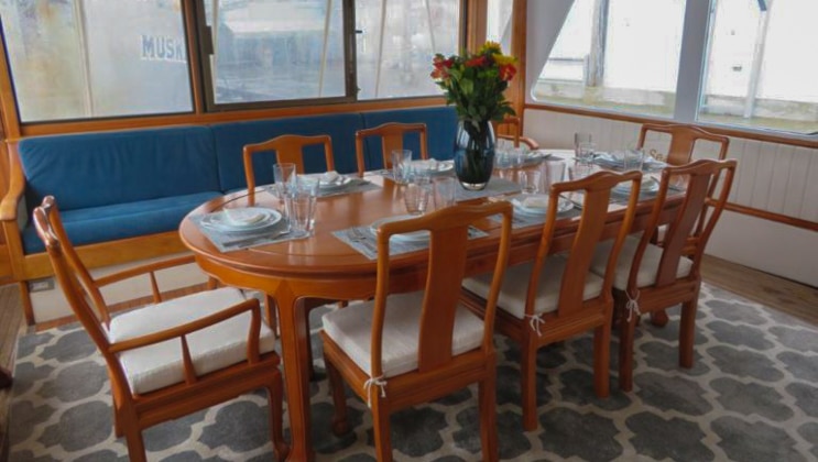 Dining room aboard the Sea Star yacht in Alaska, with wooden table set for 7 guests in a brightly lit room.