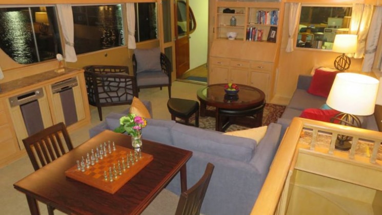 Main salon aboard the Sea Star Alaska yacht, with couches, chairs, coffee table, view windows & wooden table with 2 chairs & chess set ready for play.