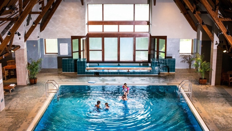 Family swims in large indoor pool with turquoise-colored water, with large Jacuzzi behind, at Hotel Alyeska near Girdwood, Alaska.