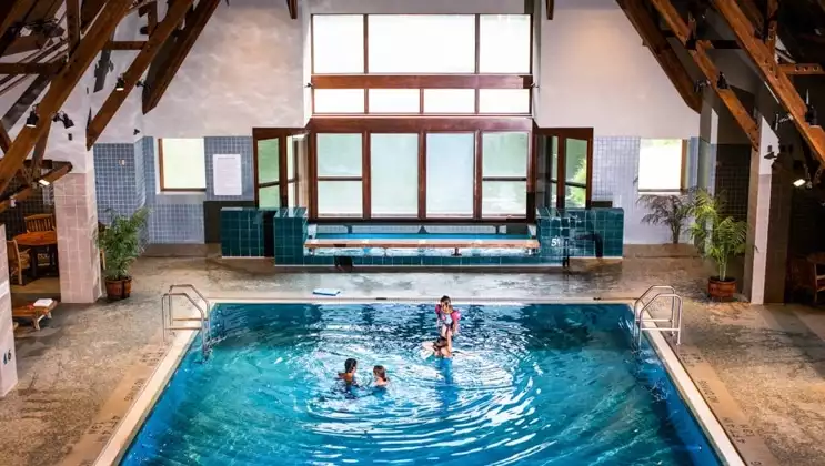 Family swims in large indoor pool with turquoise-colored water, with large Jacuzzi behind, at Hotel Alyeska near Girdwood, Alaska.