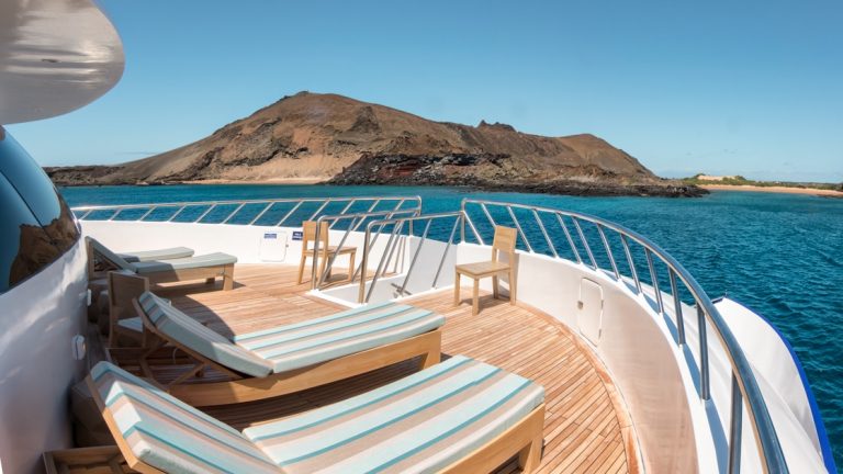 View forward from padded teal sun loungers on teak deck of M/C Endemic Galapagos cruise ship, on a sunny day.