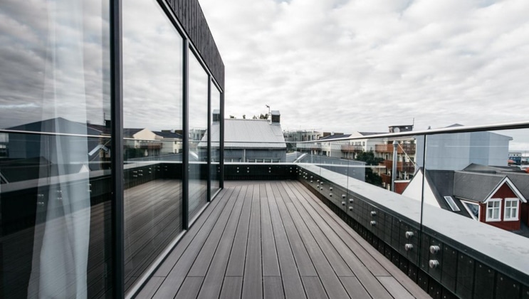 Long wraparound deck with glass railing beside walls of glass in slate gray under a cloudy sky at the Exeter Hotel in Reykjavik, Iceland.
