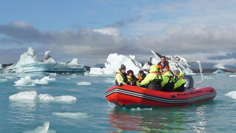 Group of Iceland Adventure travelers in dayglo green jackets Zodiac cruise among icebergs in calm water during a partly cloudy day.