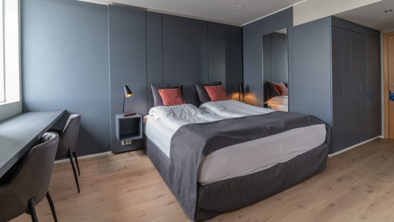 Double bed with white & gray linens in modern hotel room with gray walls & wooden floors at Hotel Isafjordur in Iceland.