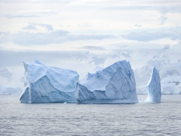 November clouds and grey light shines on a blue iceberg seen floating in Antarctica.