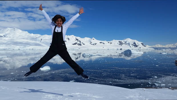 A woman in black ski overalls jumps in joy on Antarctica having reached her 7th continent in one year.