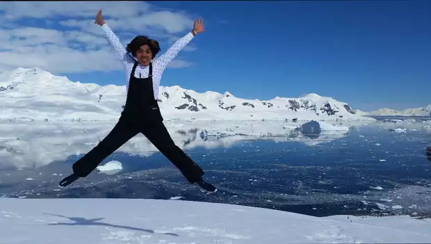 A woman in black ski overalls jumps in joy on Antarctica having reached her 7th continent in one year.