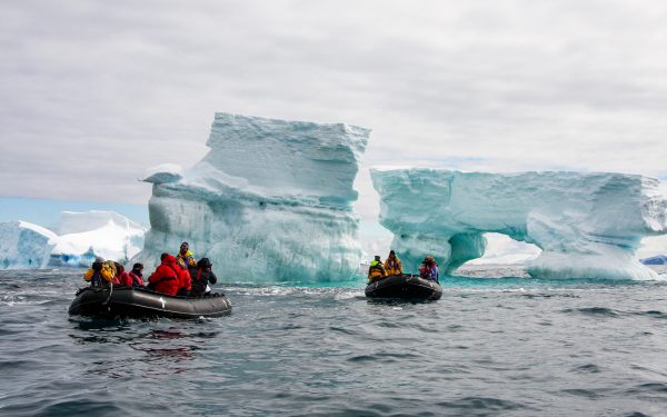 Two groups of travelers ride black inflatable zodiacs and cruise around Ice formations floating in the polar ocean water of Antarctica.