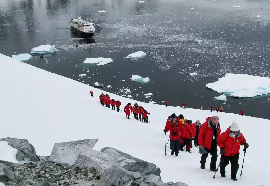 Guests wear red parkas and hike up a snowy hillside in Antarctica as part of a daily shore excursion provided by Antarctica cruise lines.
