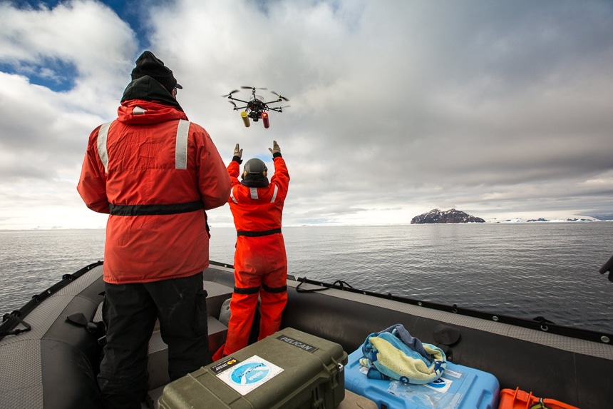 Two people wearing red parkas send a robotic drone into the air as part of scientific research program in Antarctica.