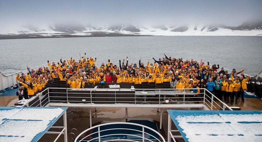 All of the guests, crew and guides from a Quark Antarctica cruise gather at the stern of the ship for a group photo in front of a snowy Antarctica mountain scape.