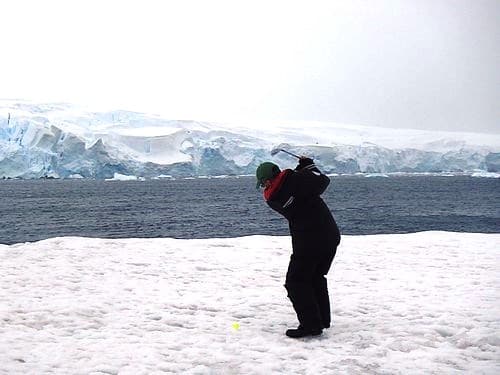 A man swings a golf club on Antarctica, celebrating having completed travel to every continent.
