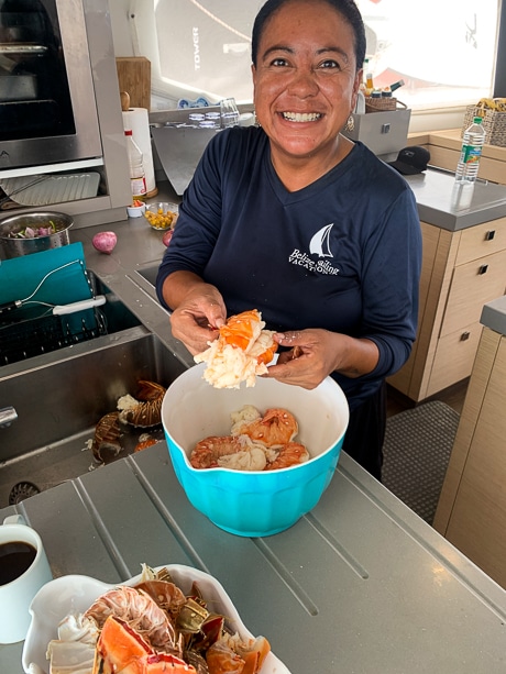 A female chef smiles as she prepares fresh caught lobster for dinner on a Belize catamaran charter.