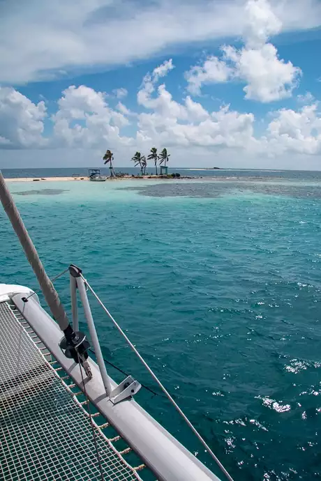 From the back deck of a Belize catamaran a tiny island of sand and palm trees sits against the teal ocean horizon.