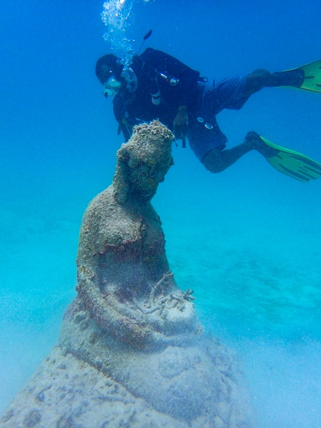 In crystal clear blue water a scuba diver swims by a submerged underwater statue in Belize.