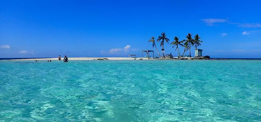 I n Belize a tiny island of sand an palm trees divides the photo with a cloudless blue sky above and crystal teal water below