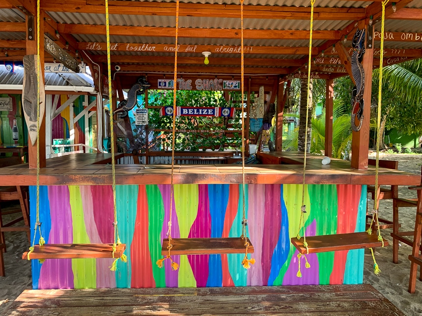 An ocean front brightly colored open air bar with swings as seats found in Plascencia in Belize.